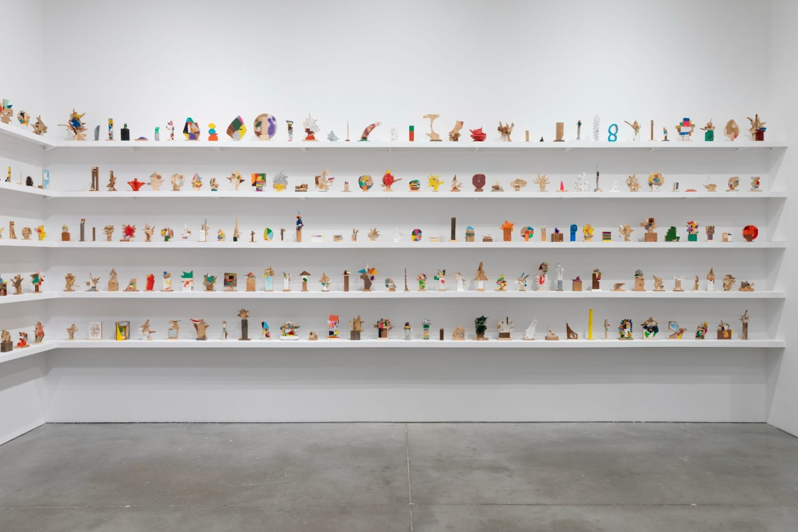 a collection of small abstract wooden sculptures painted in vibrant colors by damien hoar de galvin on white shelves