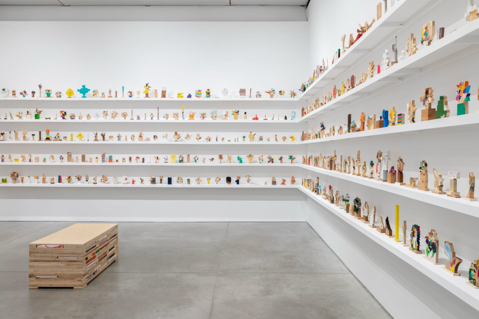 a collection of small abstract wooden sculptures painted in vibrant colors by damien hoar de galvin on white shelves