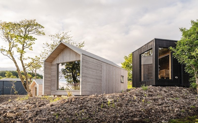 Des cabanes en bois à toit pointu s'intègrent aux reliefs écossais