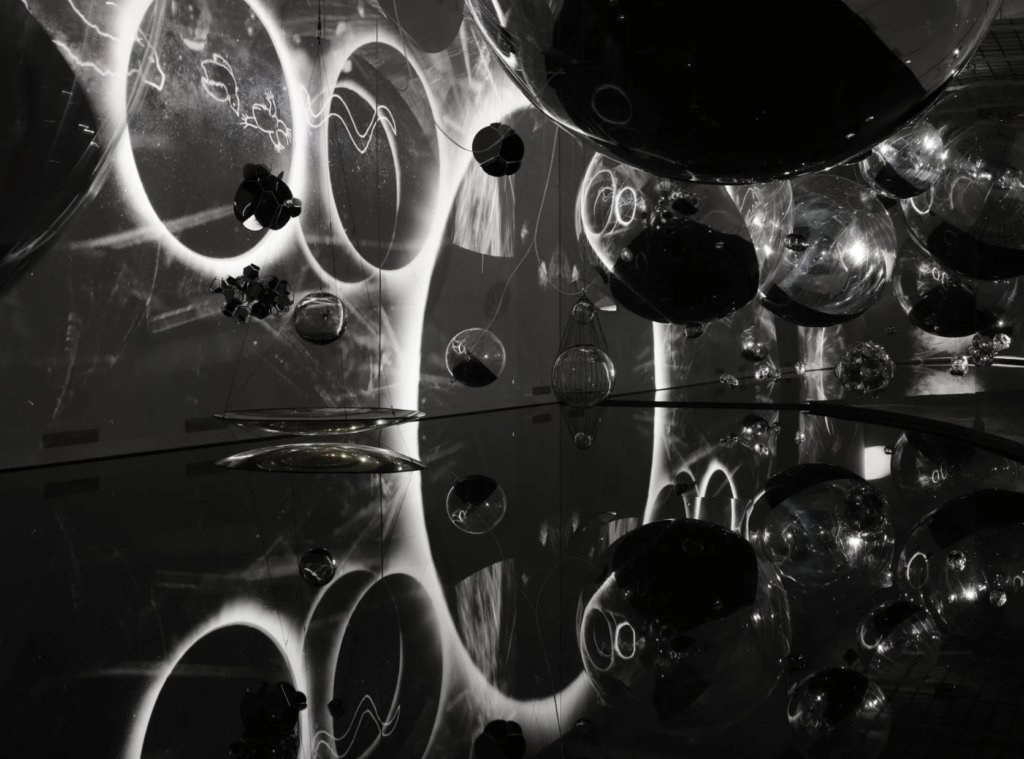 Photo en noir et blanc d'une installation artistique faite de bulles flottante à la manière d'une constellation.