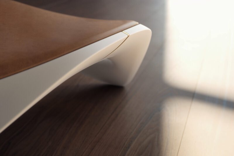 Close-up of the Ennua Element 01 chair leg with a curved white base and brown seat on a wooden floor, sunlight casting shadows nearby.